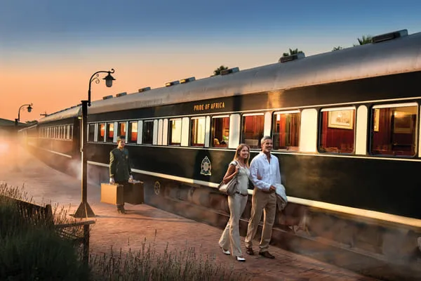 Reisende am Bahnsteig neben dem Zug „Pride of Africa“ in der Abenddämmerung